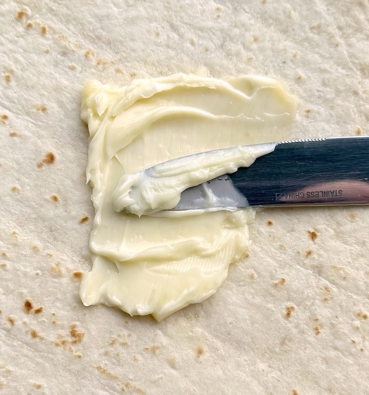 soft butter being spread onto a tortilla with a butter knife. 