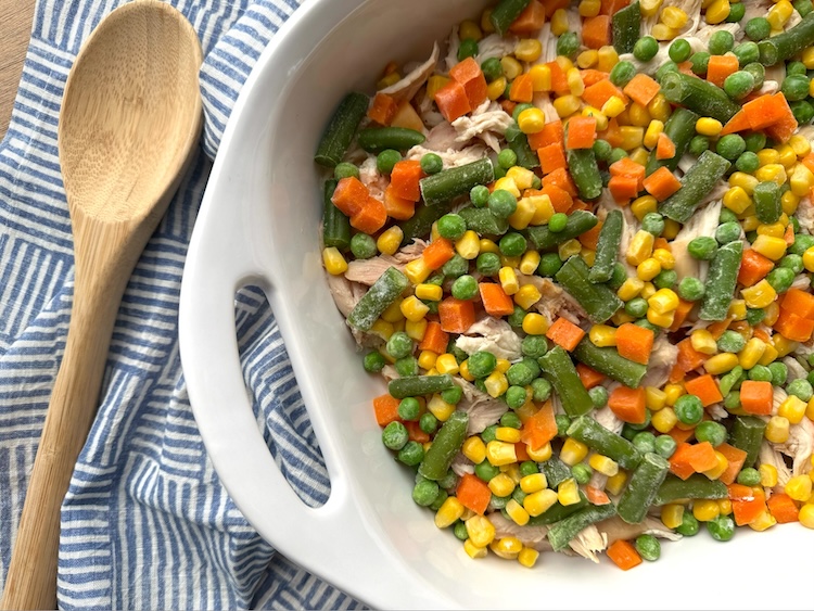 Frozen mixed vegetables in a casserole dish to make a popular chicken cobbler for dinner. 