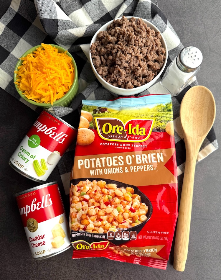 Frozen potatoes, ground beef, canned soup, shredded cheese, and seasoning all layed out on a counter ready to make a cheesy beef and potato casserole dinner.