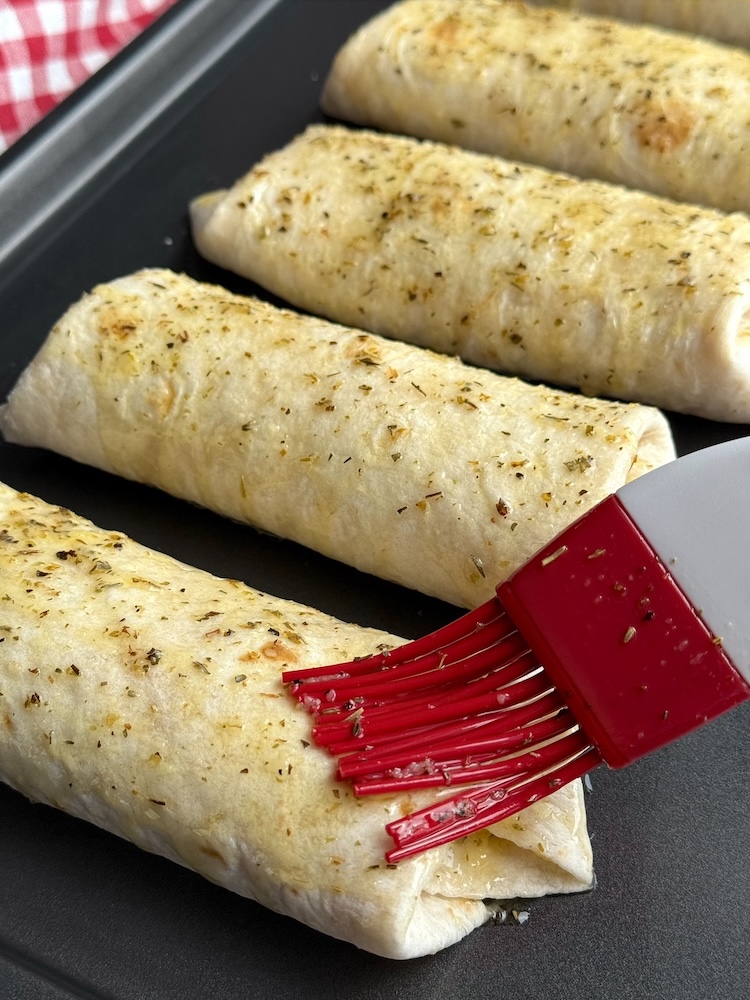 Pizza burritos on a sheet pan covered in garlic butter ready to go into the oven. 