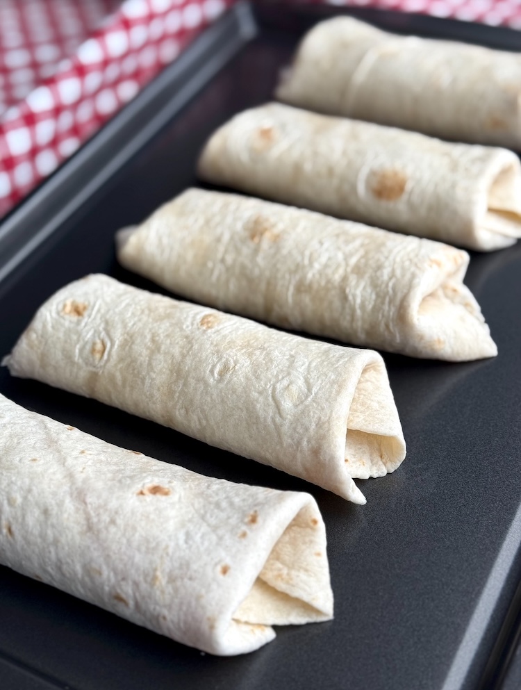 Pizza burritos rolled and stuffed in flour tortillas on baking pan. 