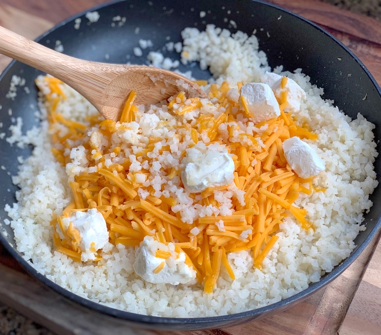 Frozen cauliflower rice in a pan with cheddar and cream cheese to make an easy, last minute side dish to serve with chicken or steak. 