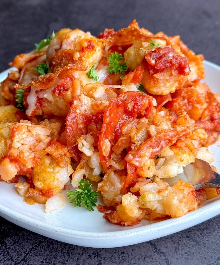 Tasty pizza casserole made with frozen tater tots on a plate ready to eat. A comfort food dinner for a family with picky eaters that can be customized with lots of different pizza toppings. 