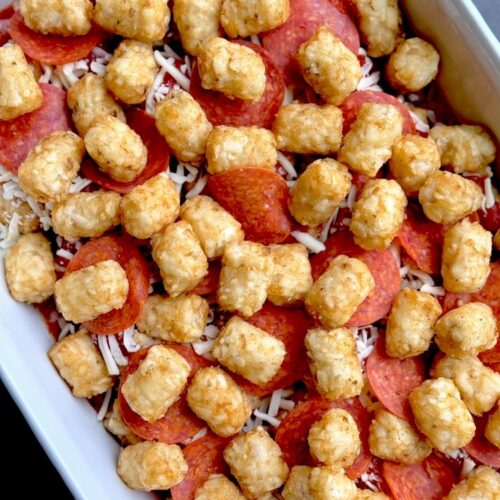 Frozen tater tots, pasta sauce, pepperoni, and mozzarella cheese all layered in a 9x13 baking dish ready to be baked in the oven.