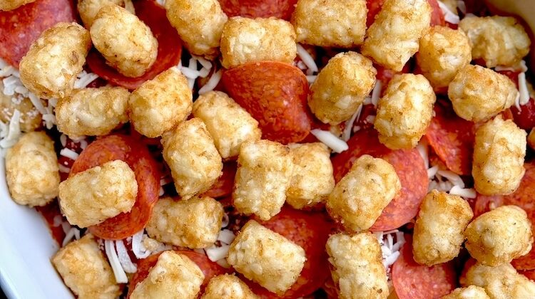 Frozen tater tots, pasta sauce, pepperoni, and mozzarella cheese all layered in a 9x13 baking dish ready to be baked in the oven.