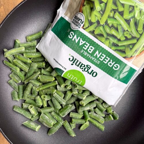 Frozen green beans being dumped out of their bag into a skillet to be steam and sautéed.