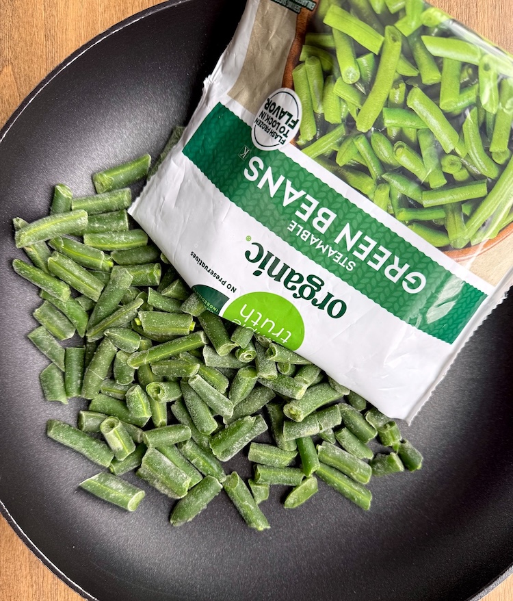 Frozen green beans being dumped out of their bag into a skillet to be steam and sautéed. 