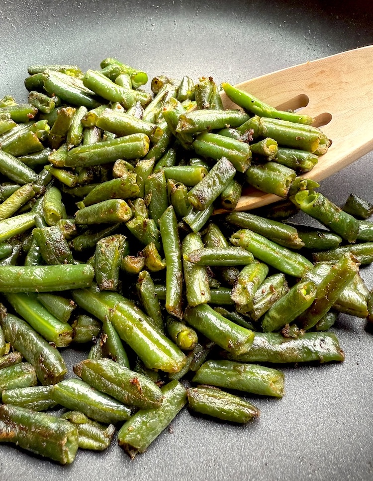 Frozen green beans in a pan sautéed with butter, oil, garlic, and other seasonings. 